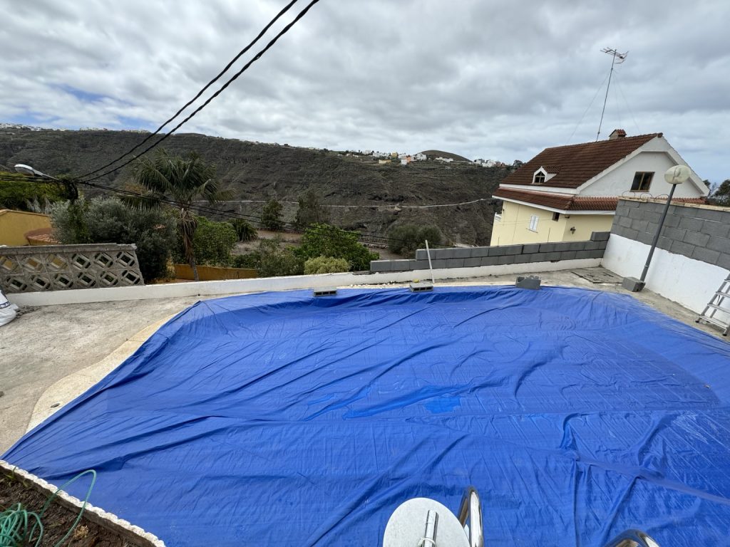 Piscina protegida con lona azul y muro perimetral en construcción