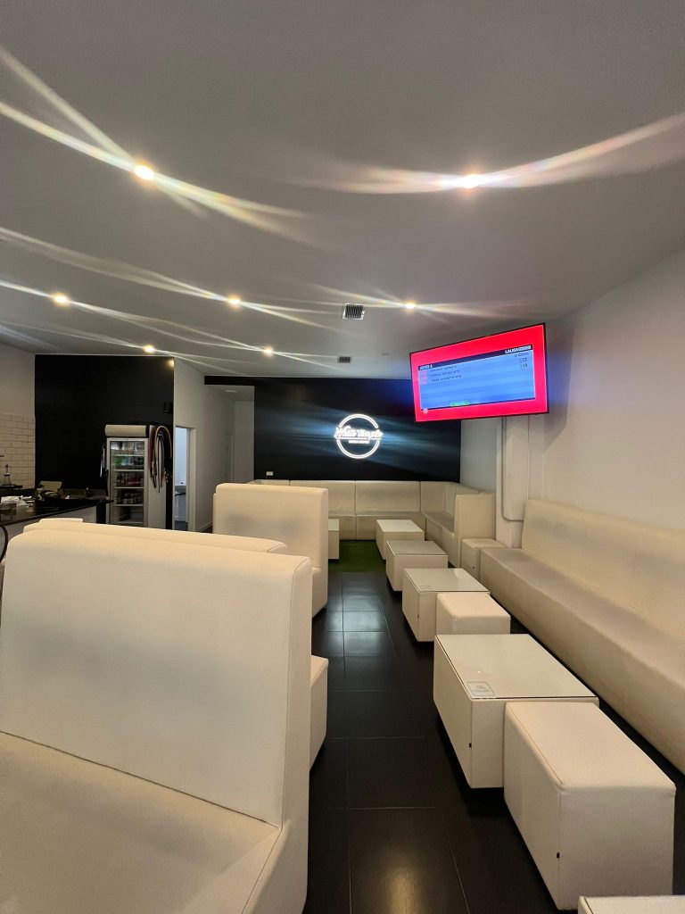 Interior de local comercial con sillones blancos, televisión y techo iluminado