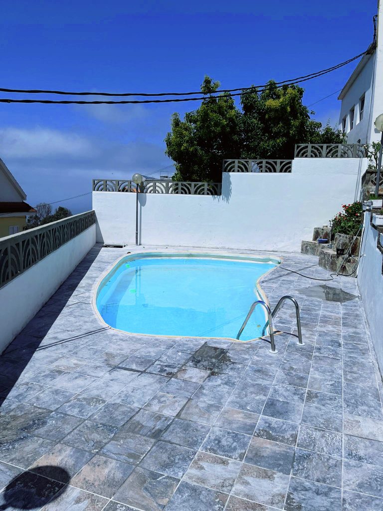 Pavimento gris alrededor de una piscina con cerramiento blanco