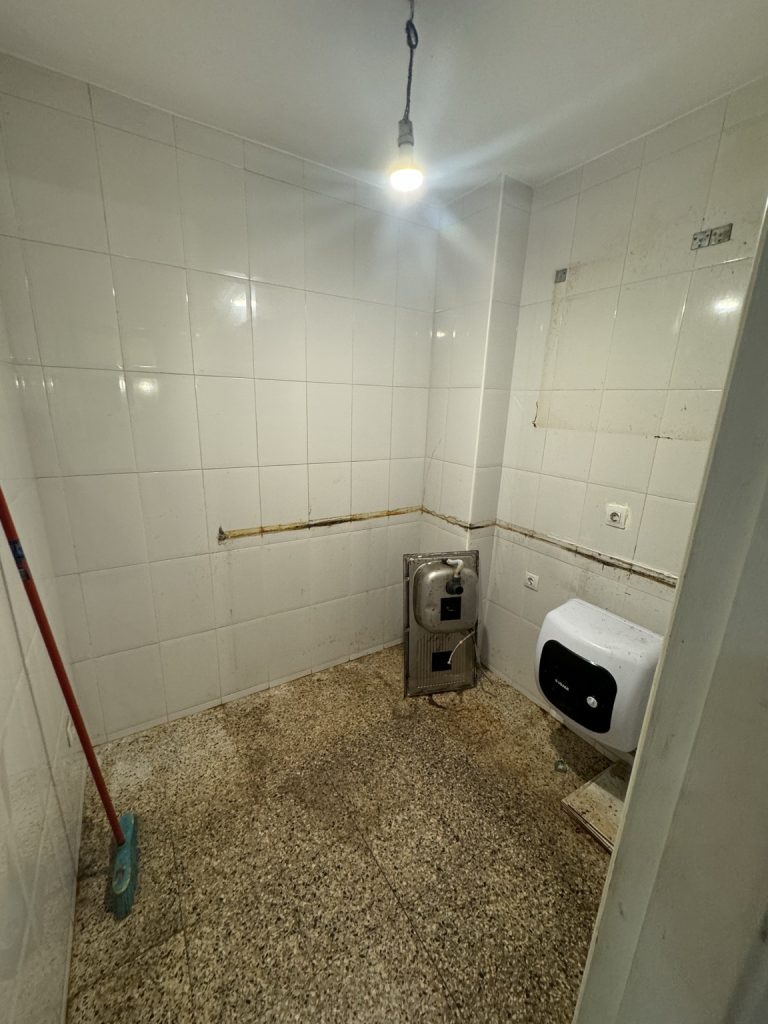 Estancia alicatada antes de reformar, con fregadero desmontado y suelo de terrazo