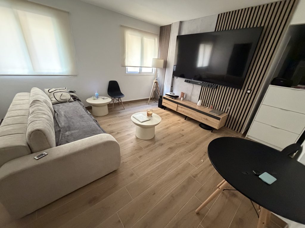 Salón con sofá blanco, televisión sobre panel de listones y suelo de efecto madera