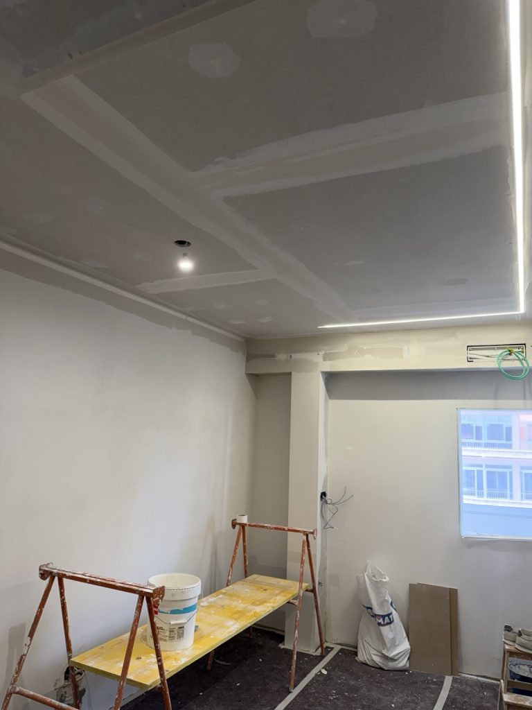 Estancia en obras con techo de placas, juntas visibles y materiales de trabajo