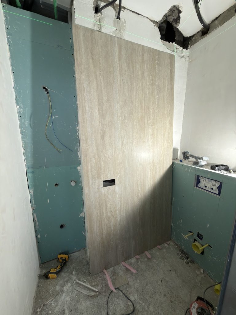 Baño en obras con revestimiento de efecto madera, placas y conexiones de fontanería