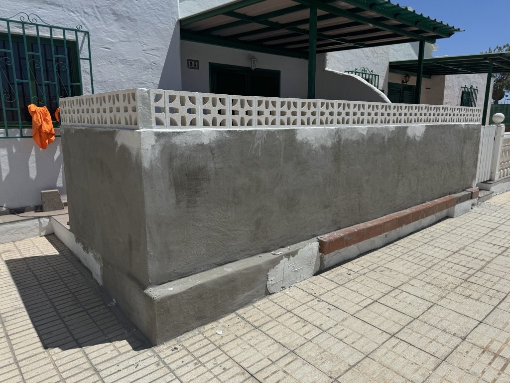 Muro exterior enfoscado junto a la acera y cerramiento de una vivienda