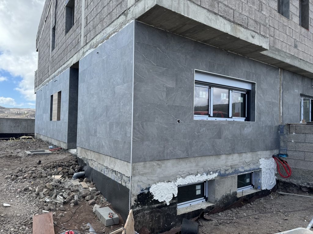 Fachada de vivienda en construcción con enfoscado gris y ventana instalada