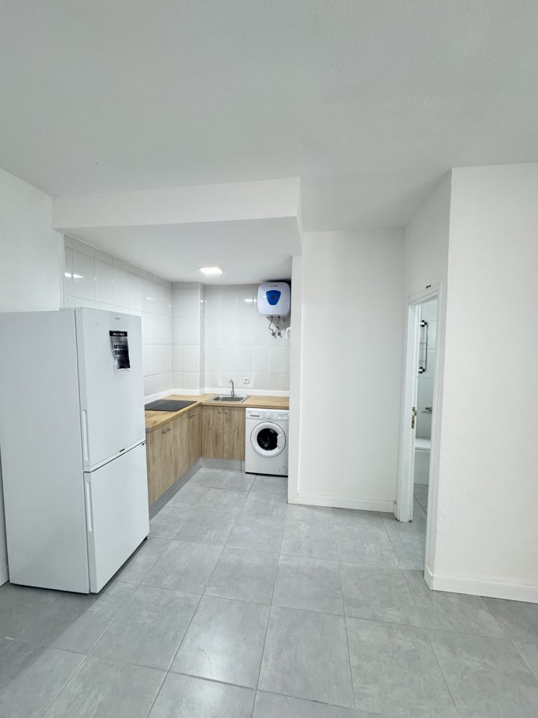 Cocina con muebles blancos, encimera de madera, frigorífico y lavadora